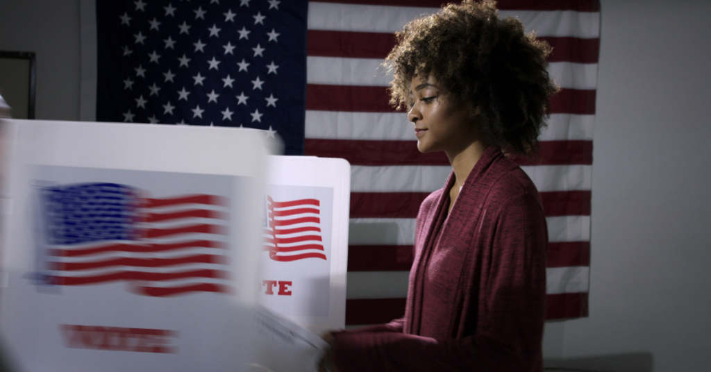 Young mixed-race woman ready to vote with blurred voting booth in foreground, being removed.