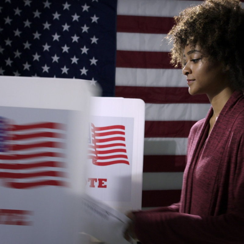 Young mixed-race woman ready to vote with blurred voting booth in foreground, being removed.
