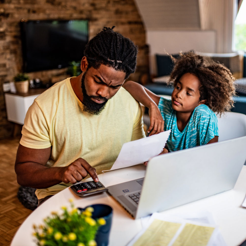 Frustrated African American man doing home finances with little daughter in the living room