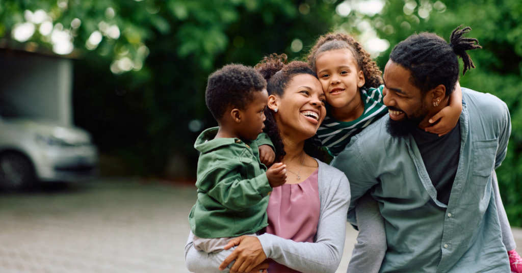 Happy African American parents spending time with their small kids outdoors