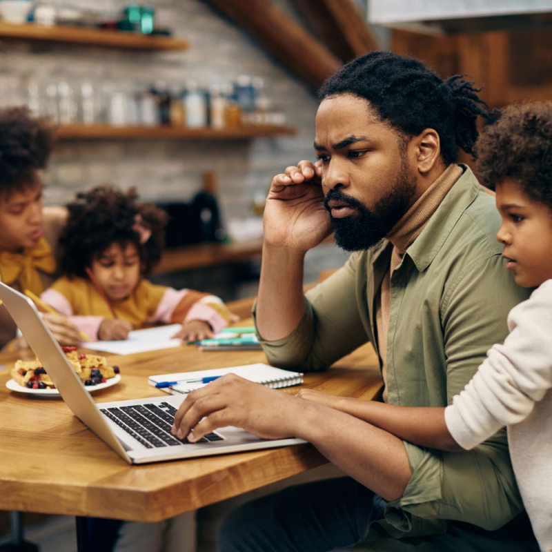 African American father reading problematic e-mail on laptop while working at home.