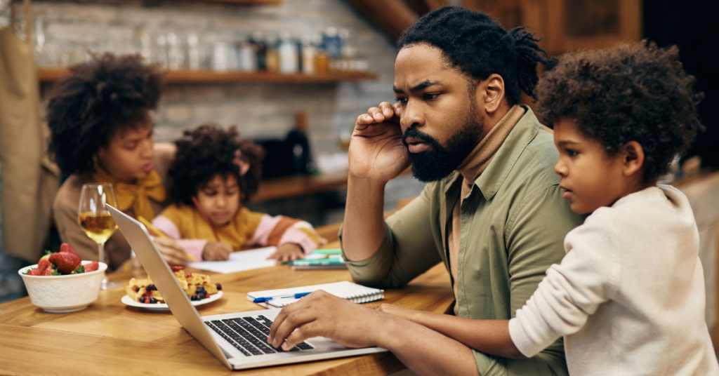 African American father reading problematic e-mail on laptop while working at home.