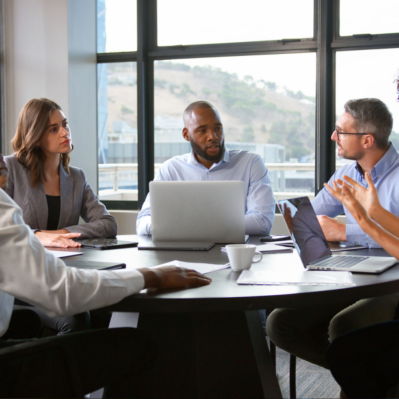 Multi-Cultural Business Team Meeting Collaborating Sitting Around Table In Modern Office Together